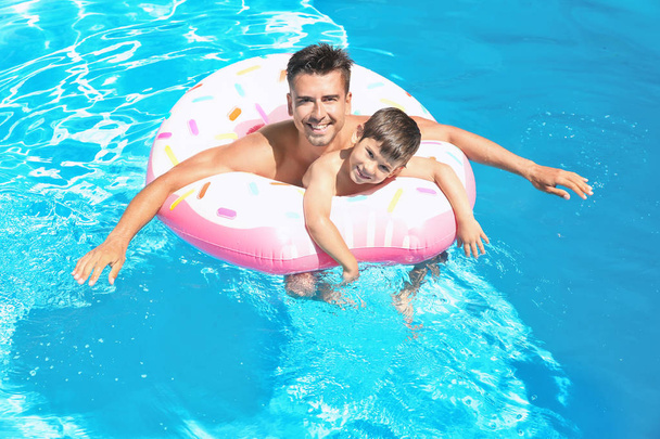 Handsome man and cute son with inflatable ring in swimming pool - Foto, afbeelding