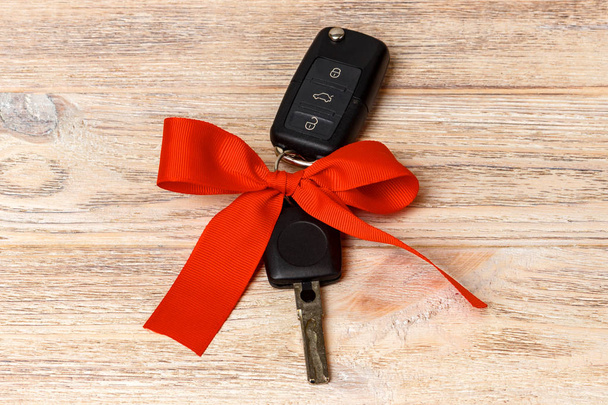 Nahaufnahme von Autoschlüsseln mit roter Schleife als Geschenk auf hölzernem Hintergrund - Foto, Bild