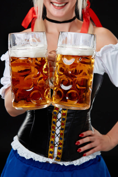 Young sexy woman wearing a dirndl with two beer mugs on black background. - Foto, imagen