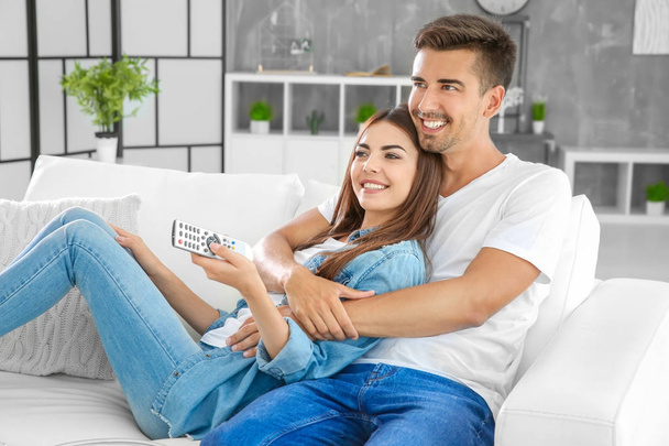 Young couple watching TV on sofa at home - Foto, afbeelding
