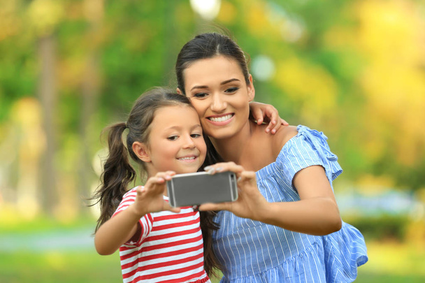 Cute little girl and mother taking selfie in park on sunny day - 写真・画像