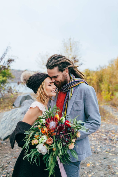 Portrait of affectionate newlyweds touching by their noses. Bride and groom posing on nature. Autumn wedding ceremony - Photo, Image