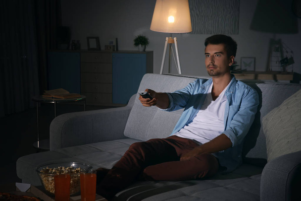 Young man watching TV on sofa at night - Foto, Bild