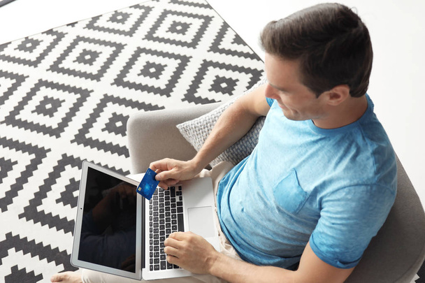 Young man holding credit card while using laptop at home - Fotoğraf, Görsel