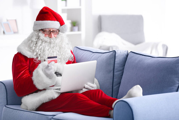 Santa Claus with laptop and credit card on sofa at home - Photo, Image