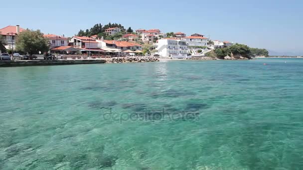 Rocky shallows with crystal clear water and beautiful settlement over blue sea - Footage, Video
