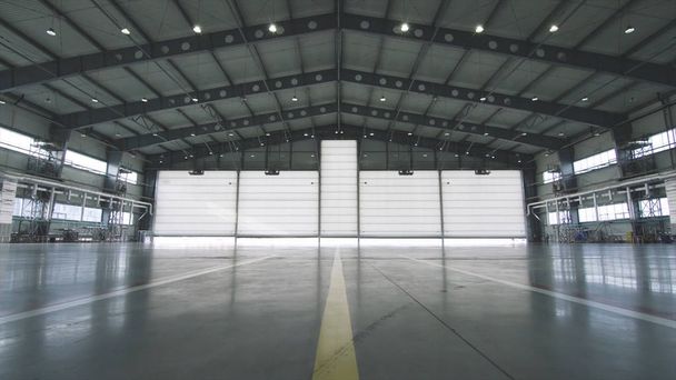 Рольставни двери и бетонный пол внутри здания завода для промышленного фона. Самолет перед полуоткрытой дверью ангара. Открытая дверь ангара. Механик открывает дверь
 - Фото, изображение
