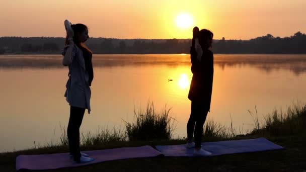 una chica embarazada hace un ejercicio de yoga con su entrenador en una orilla del lago al atardecer en Slo-Mo
 - Imágenes, Vídeo