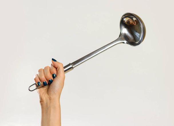 Female hands holding a metal ladle. Isolated on gray background. - 写真・画像