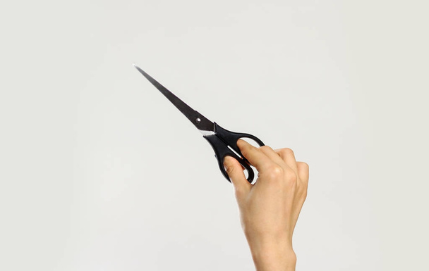 Female hands holding black scissors. Isolated on gray background - Fotografie, Obrázek