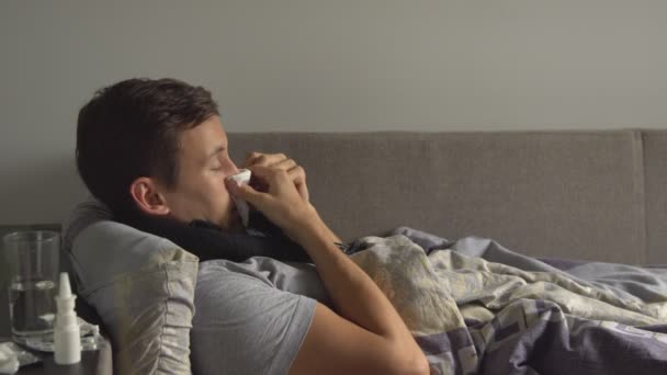 człowiek leżący chory w łóżku obok jego leki w jego domu i dmuchanie jego nos w chusteczkę - Materiał filmowy, wideo