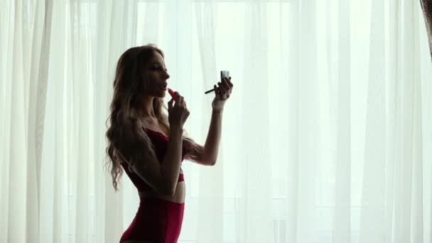 jovem vestida de roupa interior vermelha fazendo maquiagem, pinta os lábios, silhueta em backlight no fundo da janela
 - Filmagem, Vídeo