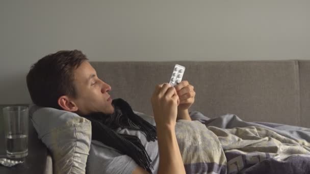 chory człowiek leżąc w łóżku obok jego leki w jego domu i bierze lekarstwo - Materiał filmowy, wideo