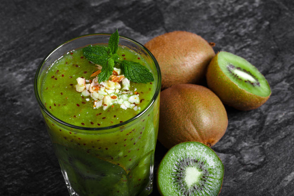 A top view of a fresh homemade kiwi smoothie with mint leaves full of nutritious vitamins on a dark gray stone background. Whole and cut kiwis near a drink. Natural cocktail for vegan breakfast. - Fotografie, Obrázek