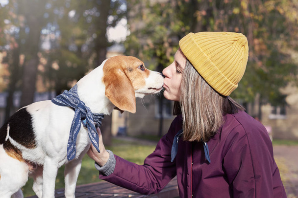 Primer plano retrato de hipster joven mujer caucásica besa a su perrito beagle. Foto al aire libre de la señora y su mascota disfrutando del buen clima otoñal. Emociones humanas positivas, expresión facial, concepto de sentimientos
. - Foto, imagen