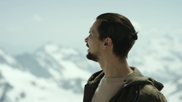 Jonge, bebaarde man op de bergtop met schilderachtig uitzicht squint ogen en kijkt rond - Video