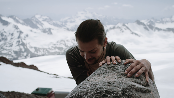 Młody facet wspinacz wejścia rock w malowniczym widokiem ośnieżonych górskich na słoneczny dzień - Materiał filmowy, wideo