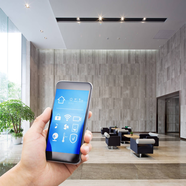 κινητό τηλέφωνο με την εφαρμογή στο έξυπνο σπίτι σε ευρύχωρη αίθουσα του κτηρίου του σύγχρονου γραφείου - Φωτογραφία, εικόνα