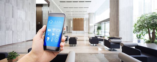mobiele telefoon met app op slimme huis in ruime hal van moderne kantoorgebouw - Foto, afbeelding