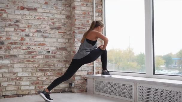 Mladá žena, která dělá protahování svalů nohou, opírající se o okenní parapet - Záběry, video