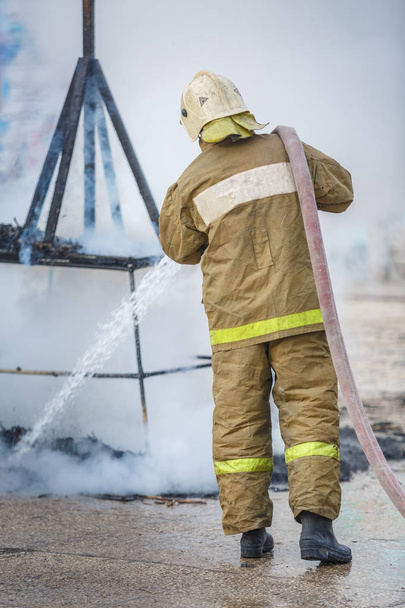 Der Feuerwehrmann löscht mit Hilfe des Hydranten mit Wasser die Brandreste im Rauch - Foto, Bild