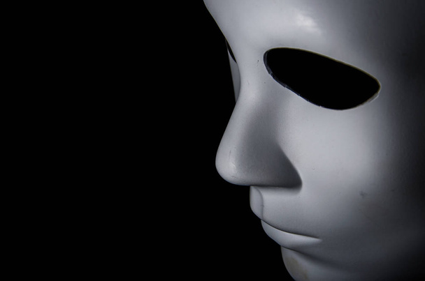 weiße Maske mit neutralem Ausdruck und Schatten auf dunklem Hintergrund. - Foto, Bild