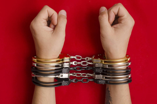 Hands in handcuffs on red background - 写真・画像