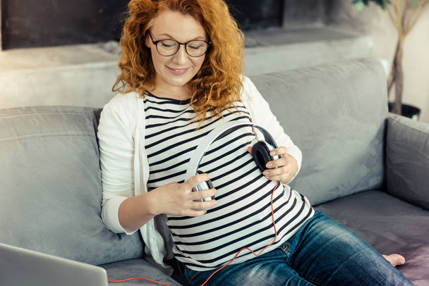 Cheerful pregnant woman keeping earphones in hands - Fotografie, Obrázek