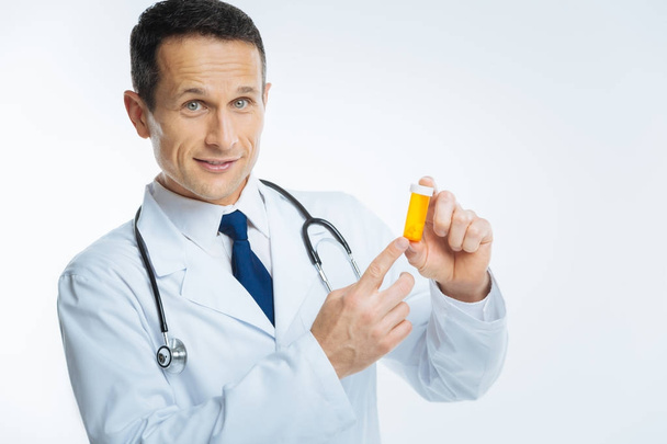 Friendly looking doctor posing with bottle of pills - Фото, изображение
