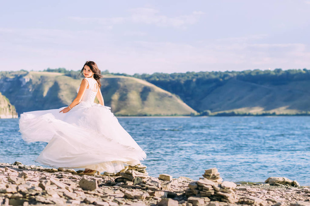 Красивая невеста в роскошном белом платье крутится вокруг озера
 - Фото, изображение