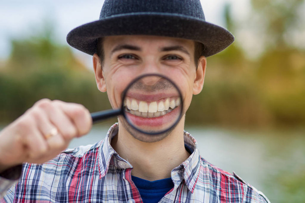 Un uomo allegro con una faccia buffa in un cappello tiene una lente d'ingrandimento
 - Foto, immagini