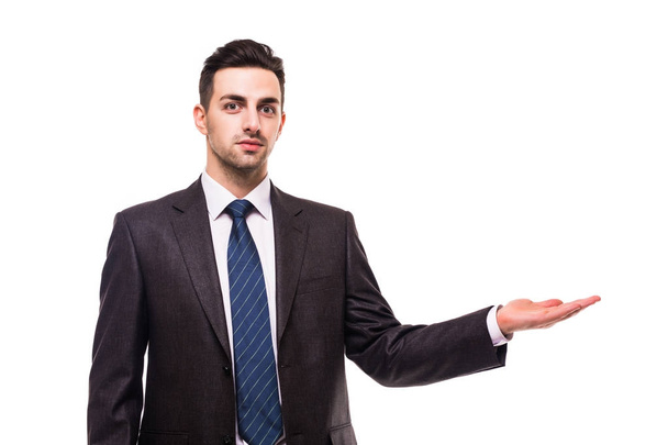 full length picture of a young business man presenting something in the back with one hand in his pocket while looking at the camera with a smile on his face, on white background - Foto, Bild