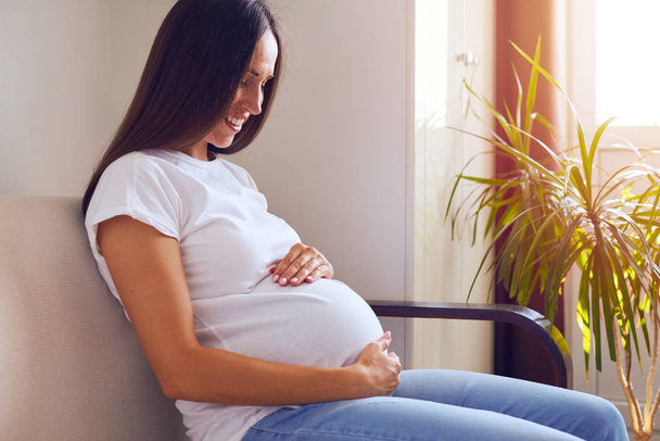 Piękna w ciąży kobieta siedzi na kanapie w domu - Zdjęcie, obraz