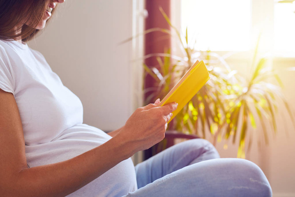 Zwangere vrouw lezen boek zittend op de Bank - Foto, afbeelding
