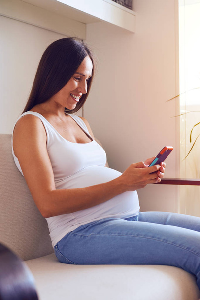Femme enceinte naviguant dans le smartphone sur le canapé
 - Photo, image