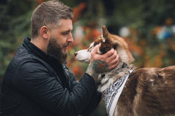 Portrait of man with a dog husky looks at each other in park at the autumn day - 写真・画像