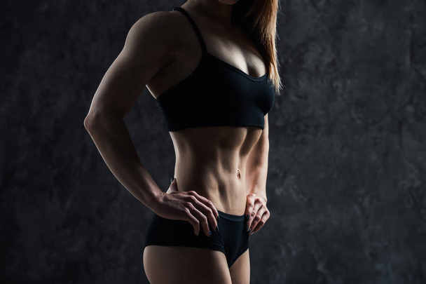 Urheilu seksikäs tyttö iso lihas vatsa musta urheiluvaatteet mustalla taustalla. Kuusisäkki vatsallaan mustan värisenä. Taut, pumpataan ylös, kiinteä vatsa
 - Valokuva, kuva