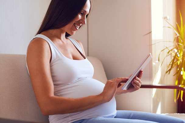 Έγκυος γυναίκα χρησιμοποιώντας tablet με ηλιαχτίδες σε φόντο  - Φωτογραφία, εικόνα