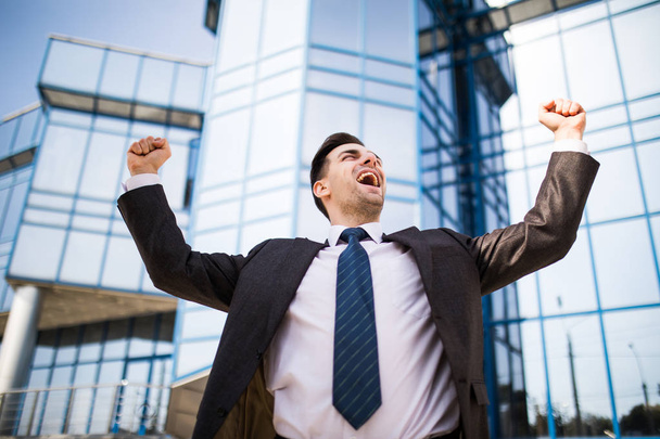 Hombre de negocios guapo levantando las armas en señal de victoria al aire libre contra el edificio de oficinas
 - Foto, imagen