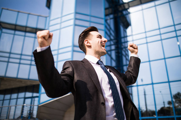 Hombre de negocios guapo levantando las armas en señal de victoria al aire libre contra el edificio de oficinas
 - Foto, Imagen