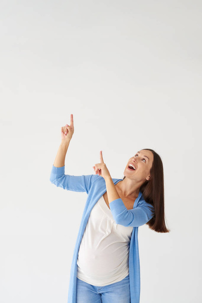 Smiling pregnant woman pointing upwards with fingers - Valokuva, kuva