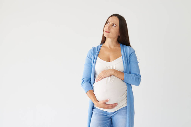 Nachdenkliche Frau hält Hand auf Schwangerschaftsbauch und schaut zu - Foto, Bild