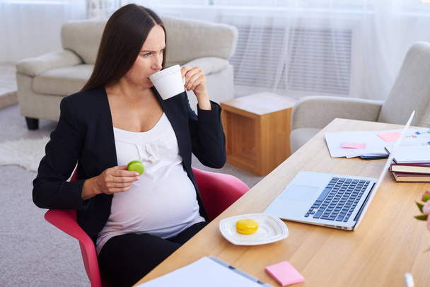 Pregnant wearing office outfit drinking tea and eating sweets - Фото, изображение