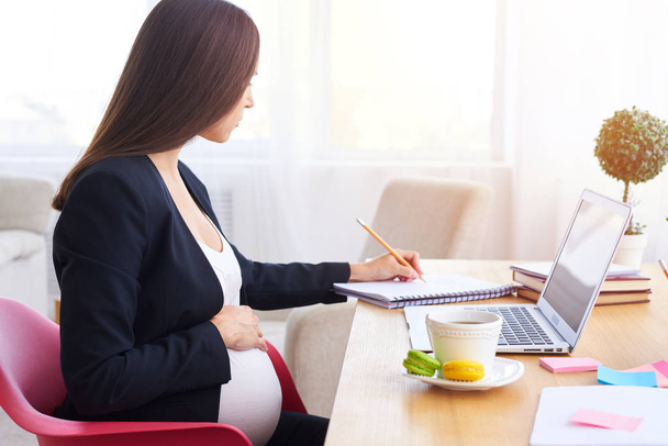 Pregnant woman holding hand on belly and making notes  - Photo, image