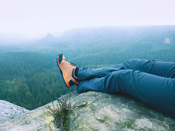 Detail of  hiker legs in black orange hiking boots on mountain summit. Feet in trekking shoes  - Фото, зображення