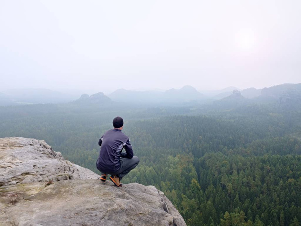 Hátulnézet egyedül természetjáró sötét szabadtéri öltöny szélén ül. Éles sziklás csúcs-völgy hegyek felett - Fotó, kép