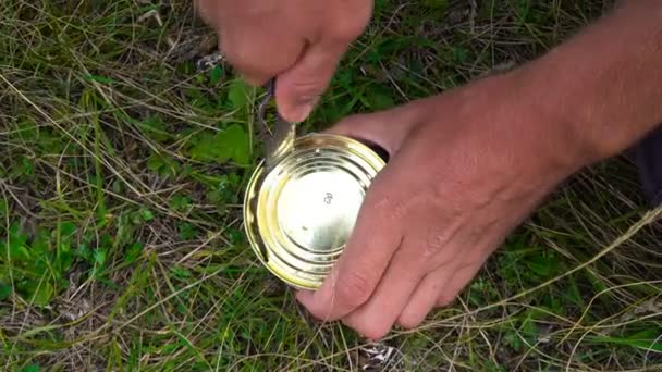 Sterke mens handen openen een ijzeren pot met vis met behulp van mes op het gras, close-up te schieten op de top. - Video