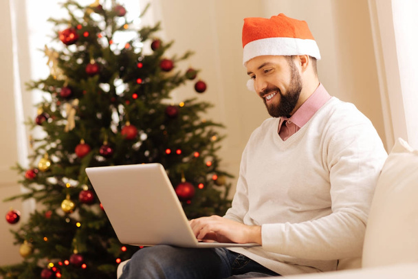 Pleasant man in Santa hat working on laptop - Photo, image