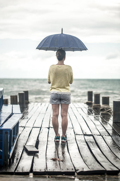 a young girl on a pier with an umbrella - Фото, зображення