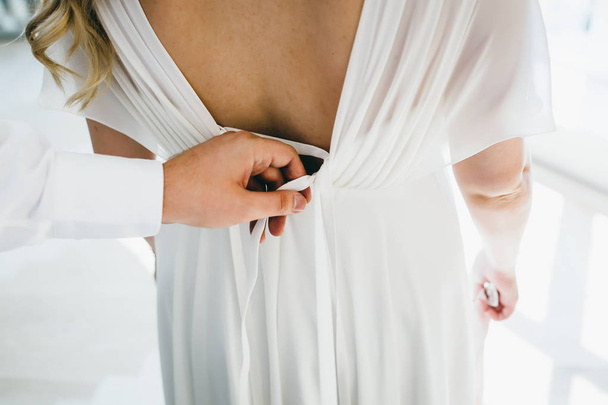 Groom helps fasten a wedding dress the bride before the ceremony. Wedding concept. Close-up Artwork - Фото, изображение